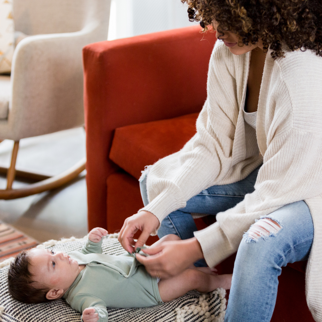 Mutter, die ihr Baby anzieht baby richtig anziehen: Eine lächelnde Mutter schließt die Knöpfe an der Kleidung ihres Babys