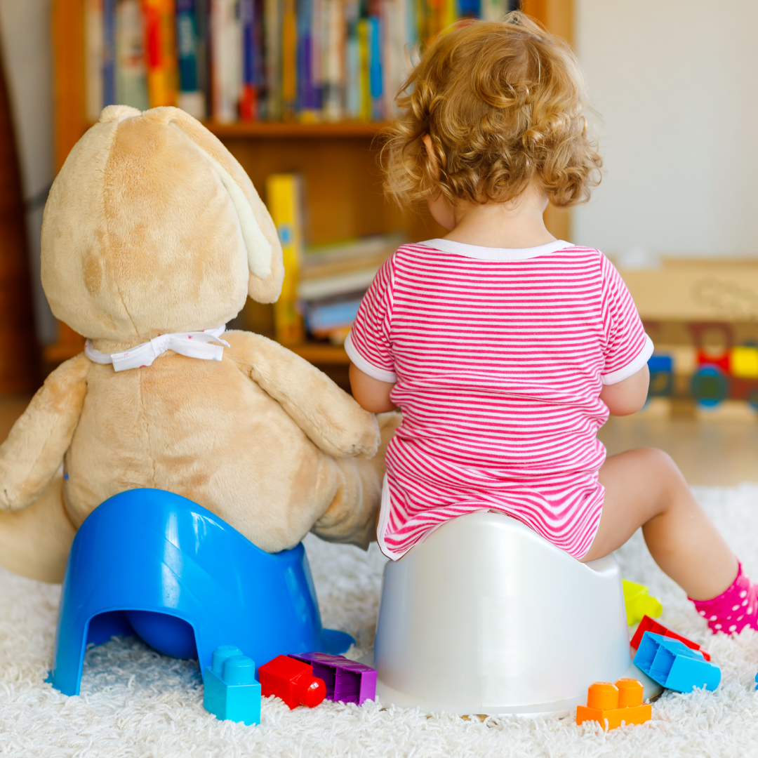 ein Kleinkind und sein Teddybär beim Töpfchentraining Ein Kleinkind sitzt Seite an Seite auf ihrem Töpfchen mit ihrem Teddybär, der von der Kamera weg zeigt. Einige bunte Spielsachen liegen auf dem Boden um sie herum