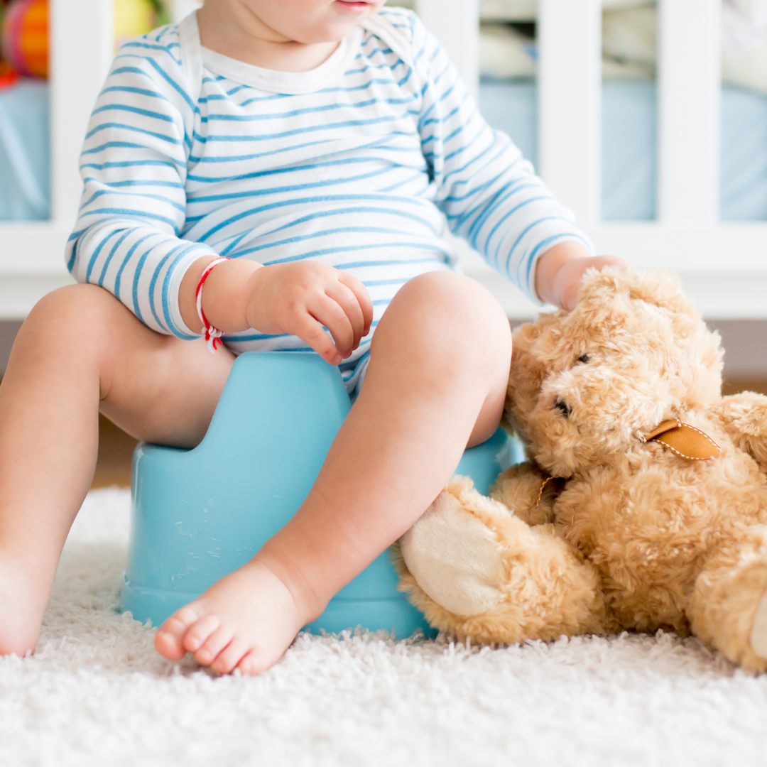 Ein Kleinkind, das in seinem Zimmer auf dem Töpfchen sitzt, während sein Teddybär neben ihm auf dem Teppich liegt 